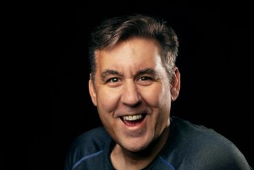 A man smiling joyfully against a black background.