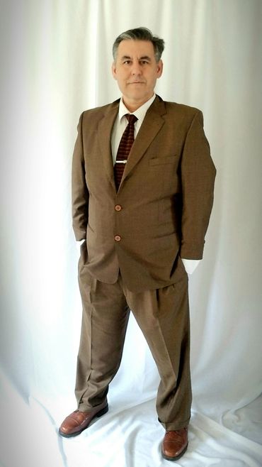 Man in a brown suit posing confidently against a white backdrop.