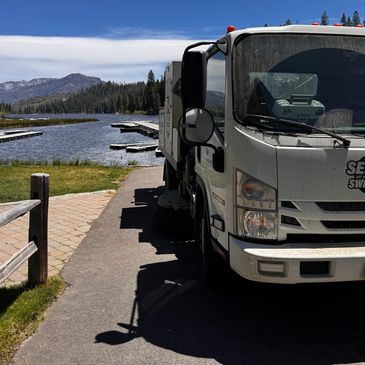 A white truck parked near a serene lakeside with mountains and forest in the background.