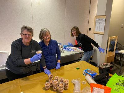 Three women preparing food with gloves on.