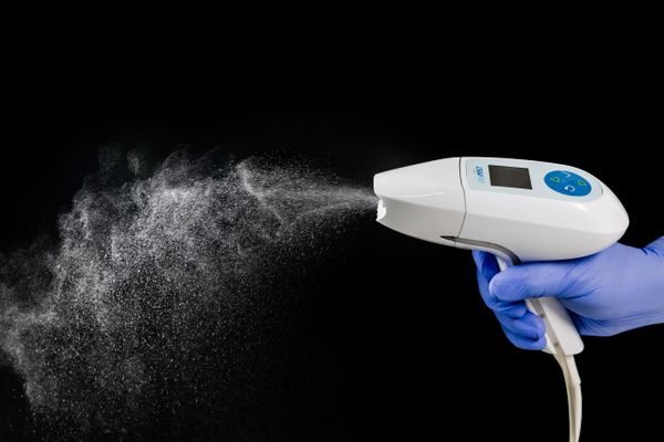 Handheld device spraying mist against black background.