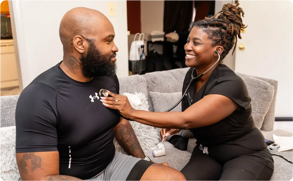 A healthcare professional listens to a man's heartbeat with a stethoscope at home.