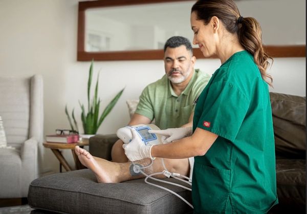 Healthcare professional checks patient's leg with medical device at home.