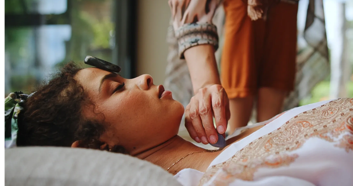 A person receiving a reiki healing crystal treatment, lying down with a stone on their forehead.
