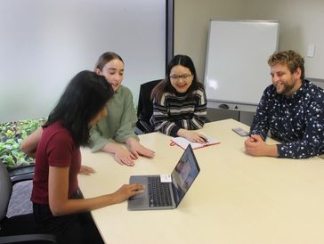 Four people engaged in a group discussion around a laptop.