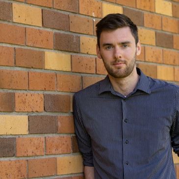 A man standing against a brick wall, wearing a striped shirt.