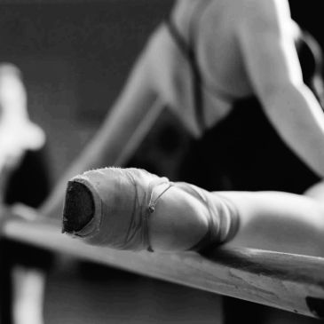 Ballet dancers practicing at the barre, focusing on a wrapped foot.