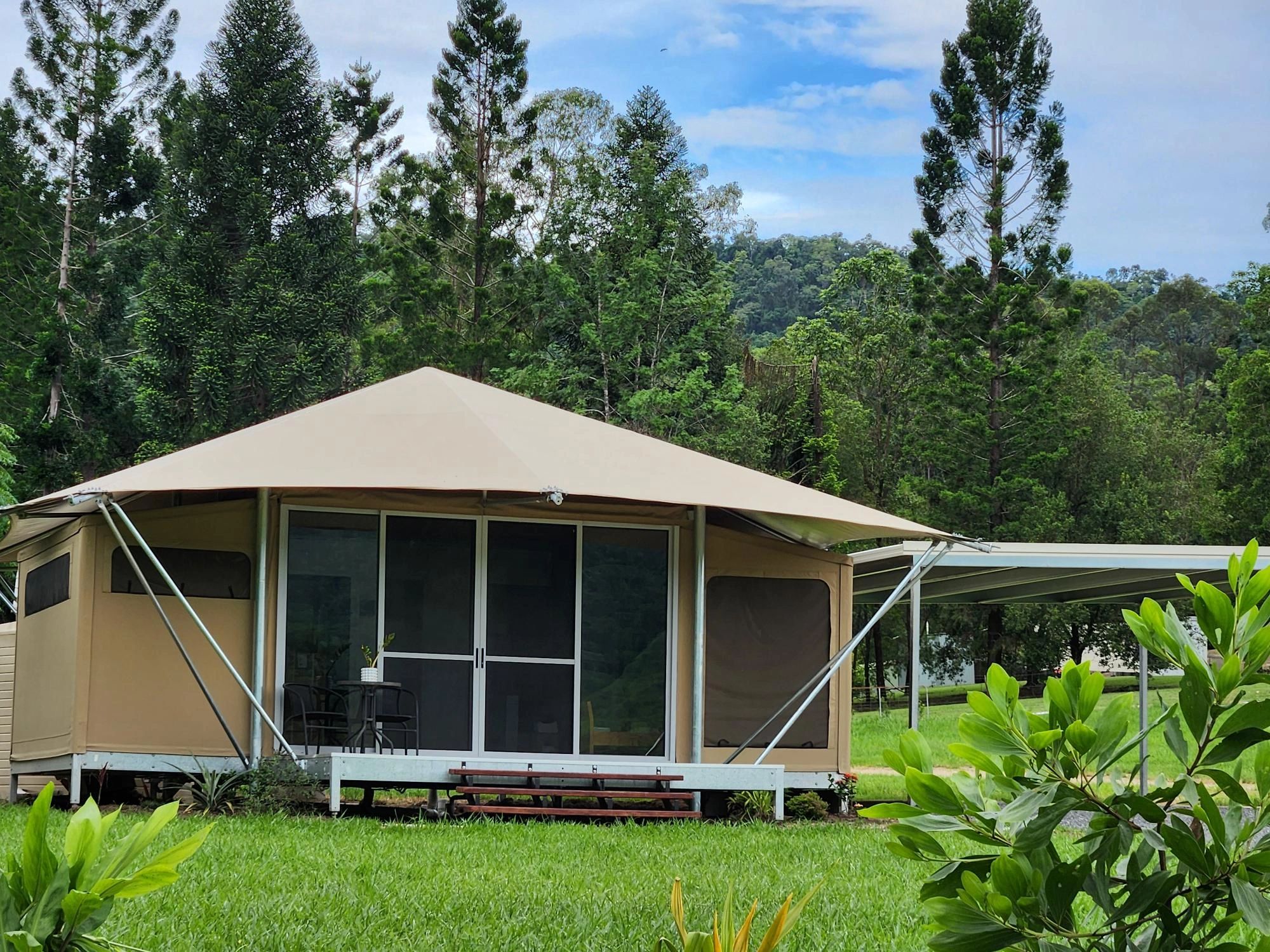 Modern glamping tent with a patio table in a lush green forest setting.