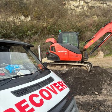 Recovery van near an orange excavator at a dirt site.