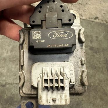 Hand holding a used Ford car sensor with wiring connector.