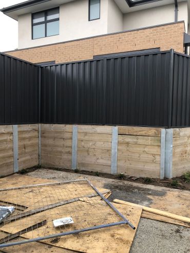 Black metal and wooden fences around a modern house under construction.