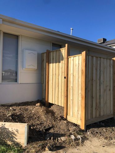 New wooden fence with gate beside a modern house under clear blue sky.