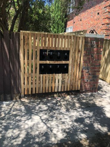 Wooden fence with eight black mailboxes numbered 1 to 8 beside a brick pillar with number 33.