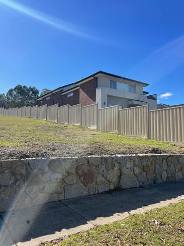 Modern house with a stone retaining wall and metal fence under a clear blue sky.