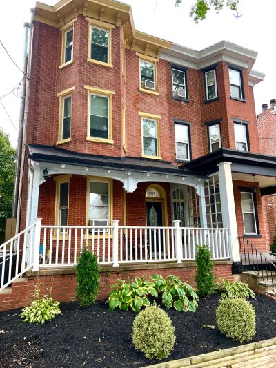 Three-story brick house with a porch and garden.