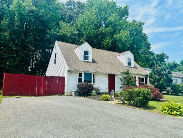 White house with red door and red fence surrounded by greenery under a blue sky.