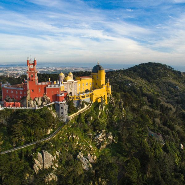 Colorful Pena Palace atop a lush green hill under a blue sky.