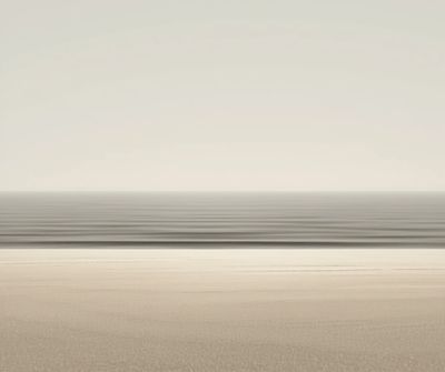 Calm, minimalist seascape with gentle waves and soft sand under a pale sky.