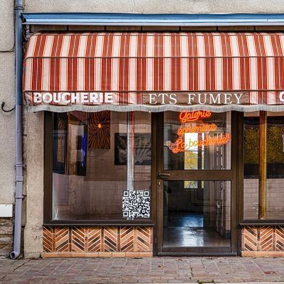 Closed butcher shop with striped awning and neon sign in French.