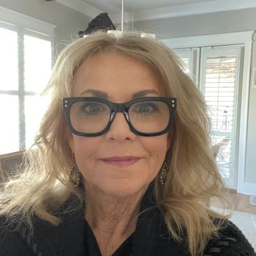 Woman with glasses smiling indoors.