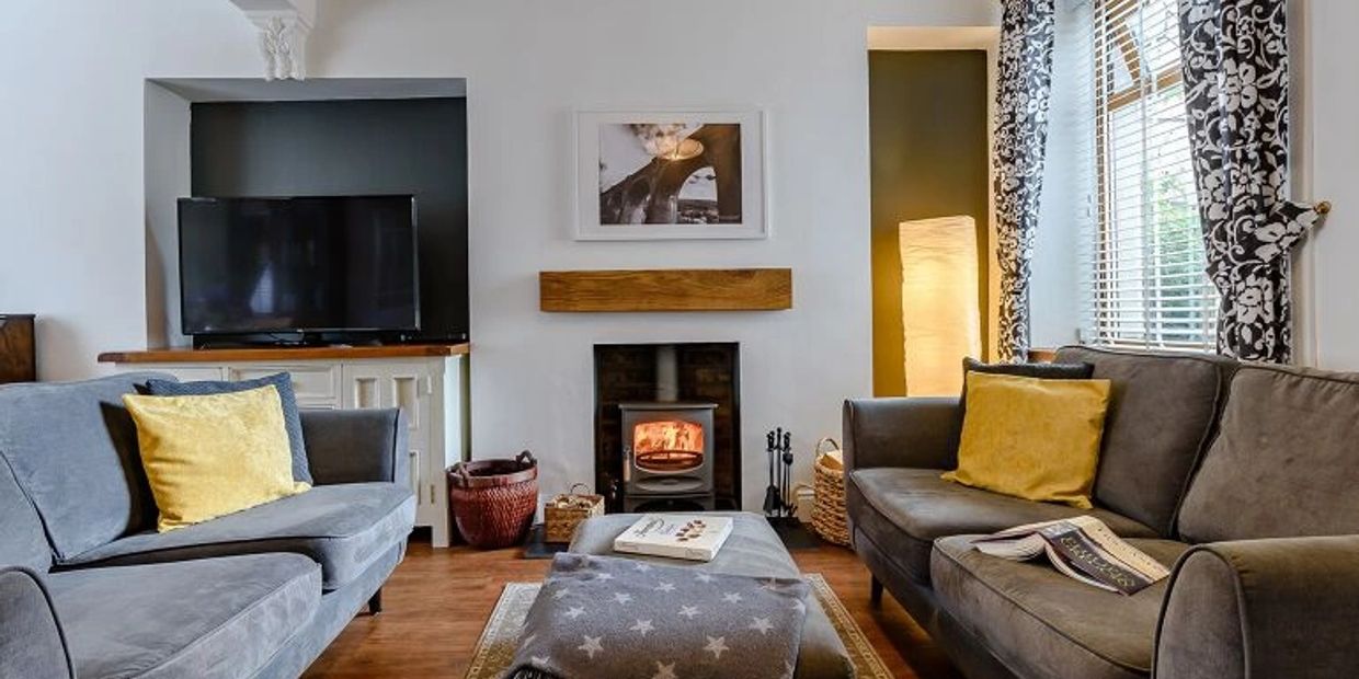 Two dark grey sofas face each other in a bright living room. Log burner in the background. 