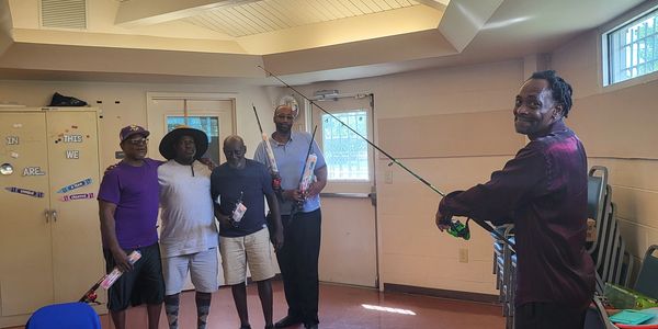 Four men posing indoors, one holding a fishing rod.