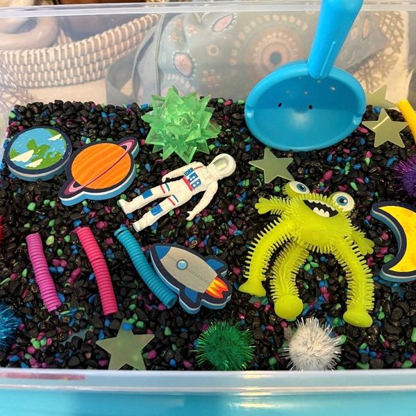 A space-themed sensory bin with toys and colorful gravel.