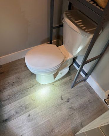 White toilet on wooden floor with metal shelving around it.