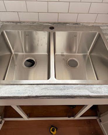 Newly installed double stainless steel kitchen sink with granite countertop.