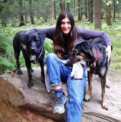 Woman sitting on a log with two dogs in a forest.