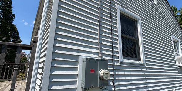 Side view of a house with electrical meter and wiring on white siding.