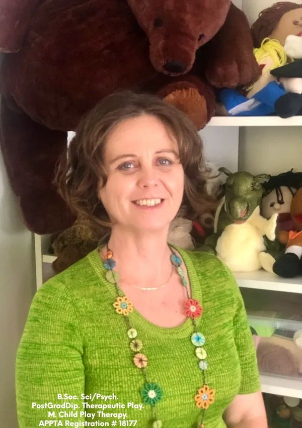 Photo of owner, middle aged female therapist, wearing a green shirt surrounded with soft toys