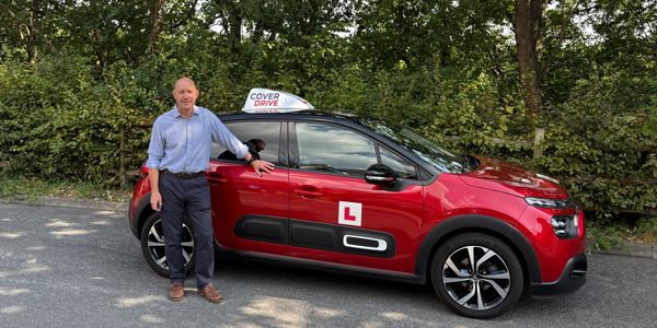 Man standing next to a red driving school car.