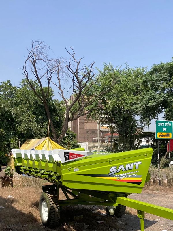 Bright green maize header trailer parked on a roadside under a clear sky.
