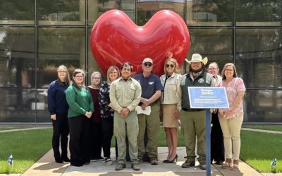 A group posing in front of a large red heart sculpture outdoors.