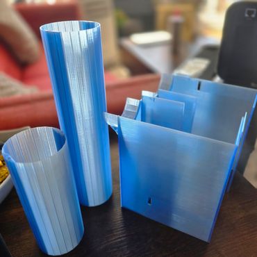 Blue 3D printed cylindrical and rectangular objects on a dark surface.