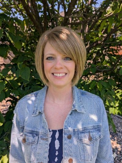 Smiling woman with short blonde hair wearing a denim jacket, standing outdoors.