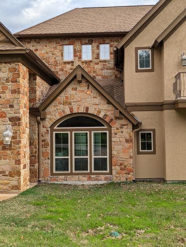 Stone and stucco house exterior with multiple windows and a green lawn.