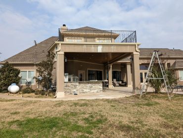 Large backyard patio with outdoor kitchen and ladder beside the house.