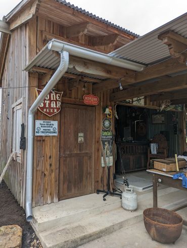 Rustic wooden building with vintage signs and outdoor items on concrete porch.