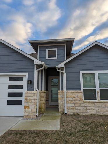 Modern house entrance with blue siding and stone accents under a cloudy sky.