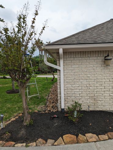 Backyard corner with a tree, garden tools, and a stone border.