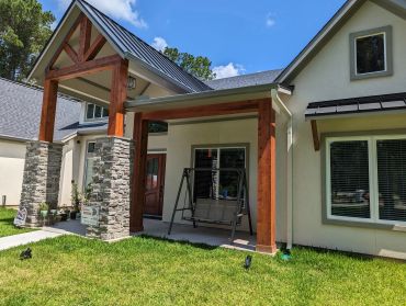 Modern house entrance with stone pillars and a wooden porch swing.