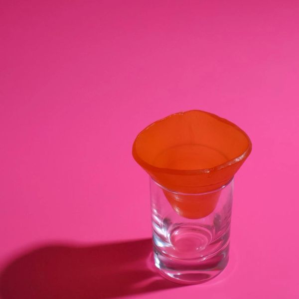 Orange silicone funnel in a clear glass on a pink surface.