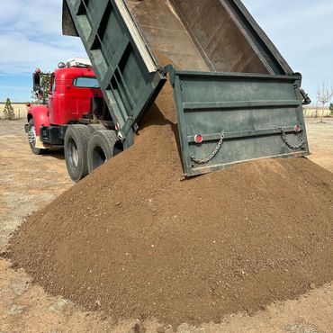 A red dump truck unloading a large pile of dirt outdoors.