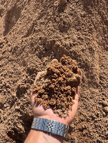 Hand holding a clump of dry, brown sand or soil under bright sunlight.
