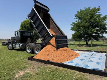 Dump truck unloading a pile of sand on a prepared ground area.