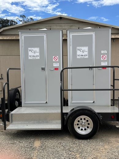 Portable restroom trailer with two doors on a trailer bed.
