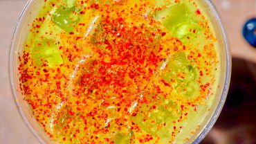 Spicy iced yellow drink with chili flakes.