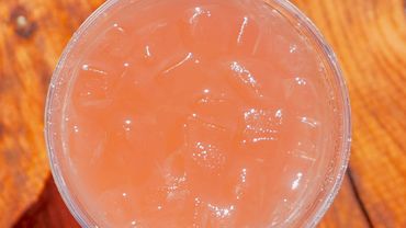 A glass of pink iced drink on wooden surface.